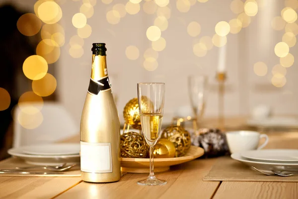 Kersttafel decor met vakantie decoraties in een gouden kleur. Nieuwjaarsfeest. Een fles en een glas champagne.. — Stockfoto