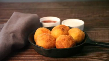 Kadın eli bir patates kroket topu alır ve sosa batırır.