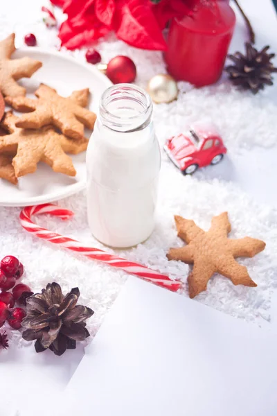 Plätzchen, Zuckerrohr, Milch für den Weihnachtsmann und leeres Blatt Papier auf dem Tisch auf dem Hintergrund der Weihnachtsdekoration — Stockfoto