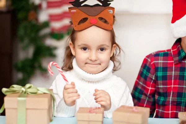 Смішна дівчина в масці різдвяних оленів тримає цукеркову тростину в руці — стокове фото