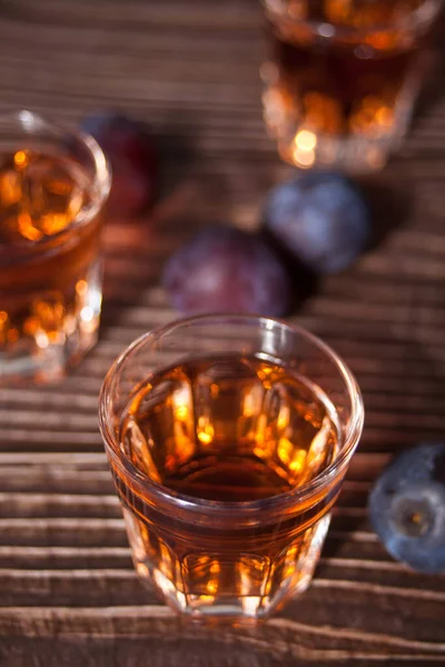 Wódka lub brandy ze świeżymi śliwkami na drewnianym stole. — Zdjęcie stockowe