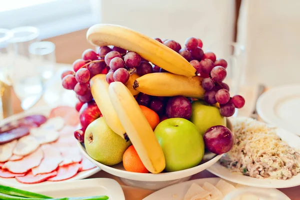 Trauben, Äpfel, Birnen, Bananen und andere Früchte in einer Vase auf einem festlichen Tisch — Stockfoto