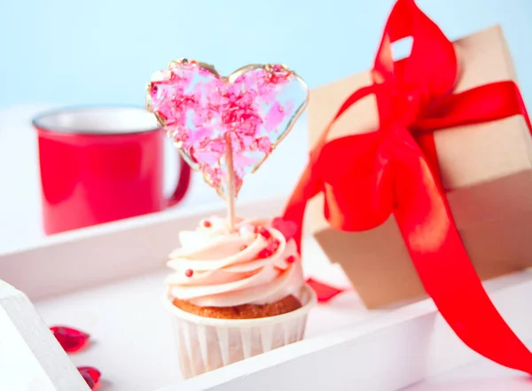 Valentine cupcake cream cheese frosting decorado com pirulito de doces do coração, caneca de café e caixa de presente no fundo. — Fotografia de Stock
