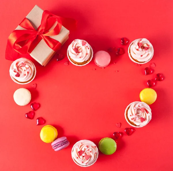 Herzförmiger Rahmen mit Cupcakes Frischkäse Zuckerguss mit Herzbonbons, Makronen, Geschenkbox verziert. Valentinstag Konzept. Ansicht von oben. Kopierraum. — Stockfoto
