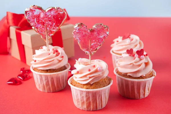 Valentines cupcakes cream cheese frosting decorated with heart candy lollipops and gift box on the background. — Stock Photo, Image