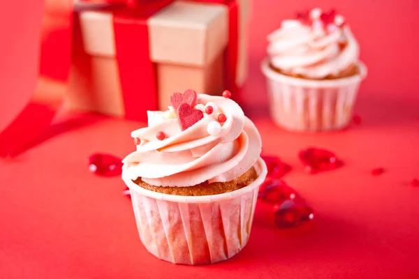 Valentines cupcakes cremă brânză înghețată decorată cu bomboane de inimă și cutie de cadouri pe fundalul roșu . — Fotografie, imagine de stoc