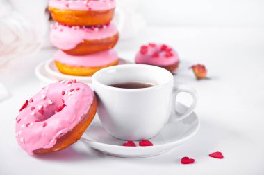 Beyaz arka planda bir fincan kahve ve pembe çörekler. Sevgililer Günü konsepti