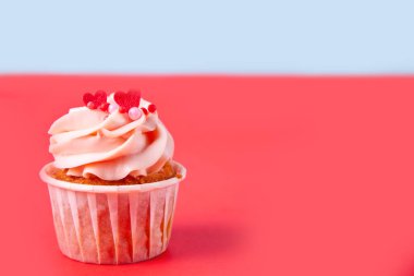 Sevgililer Günü kekleri krem peynirli krem peynir süslemesi. Kırmızı arka planda kalp şeklinde şekerler var. Boşluğu kopyala.