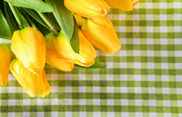 Gele tulpen over armoedig geruit groen tafelkleed. — Stockfoto