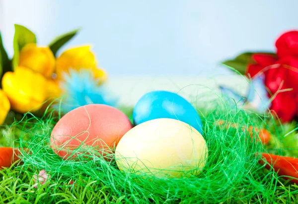 Tres huevos de Pascua decorados en la hierba con flores tulipanes en el fondo — Foto de Stock