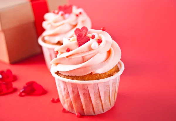 Valentines cupcakes cremă brânză înghețată decorată cu bomboane de inimă și cutie de cadouri pe fundal roșu . — Fotografie, imagine de stoc