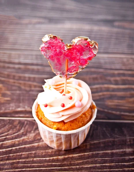 Valentine cupcake cream cheese frosting decorado com pirulito de doces cardíacos no fundo de madeira — Fotografia de Stock