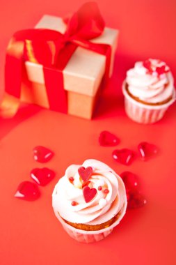 Sevgililer Günü kekleri krem peynirli krem karamela ve kırmızı arka planda hediye kutusuyla süslenmiş..
