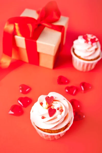 Valentines cupcakes cream cheese frosting decorated with heart candy and gift box on red background. — Stock Photo, Image