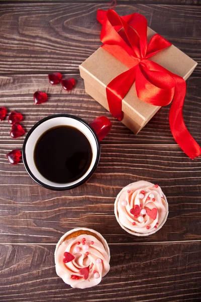 Valentines cupcakes cream cheese frosting decorated with heart candy, mug of coffee and gift box on the wooden background. — Stock Photo, Image