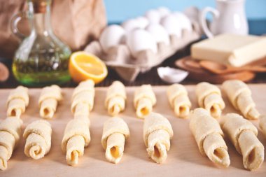 Evde kruvasan yapıyorum. Hamuru daha fazla pişirmek için rulo şeklinde yuvarlıyor. Malzemeler ve mutfak gereçleri arka planda. Üst görünüm.