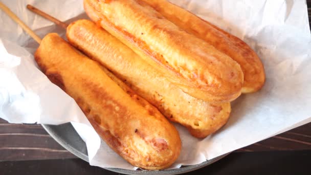 Corndogs op een stokje met ketchup en mosterd op de houten tafel. Menselijke hand schenkt saus. — Stockvideo