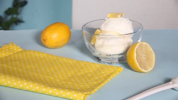 Main de femme mettre un bol avec de la crème glacée au citron frais maison avec des tranches de citron sur la table. Dessert d'été. — Video