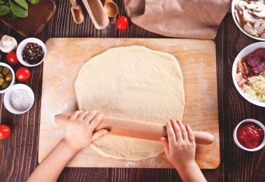 Çocuk ev mutfağında pizza hamuru yapıyor. Üst görünüm.