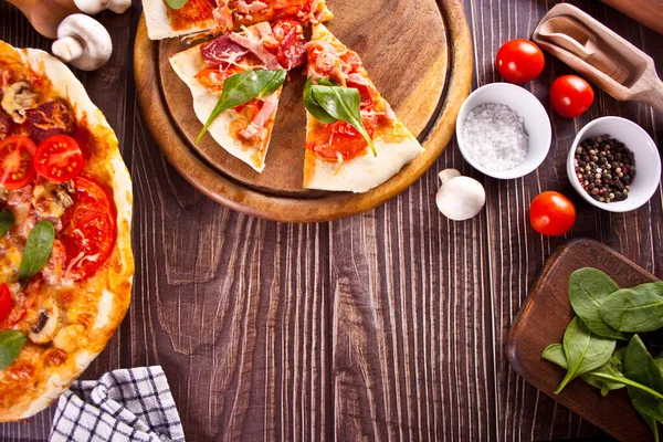 Pizza casera con salchicha de pepperoni, tocino decorado con espinacas e ingredientes en el fondo. Vista superior. Copiar espacio. —  Fotos de Stock