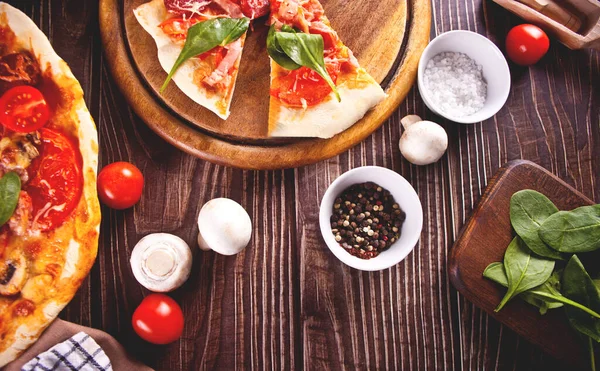 Pizza casera con salchicha de pepperoni, tocino decorado con espinacas e ingredientes en el fondo. Vista superior. Copiar espacio. —  Fotos de Stock
