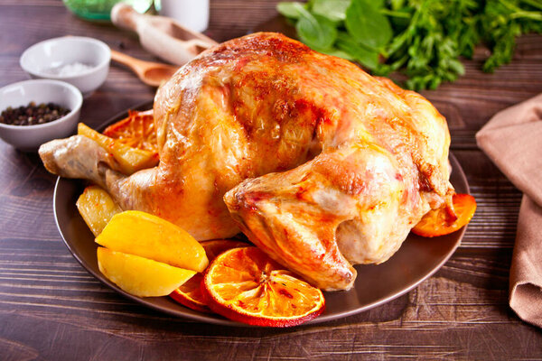 Roasted whole chicken with oranges and potatoes on a plate.