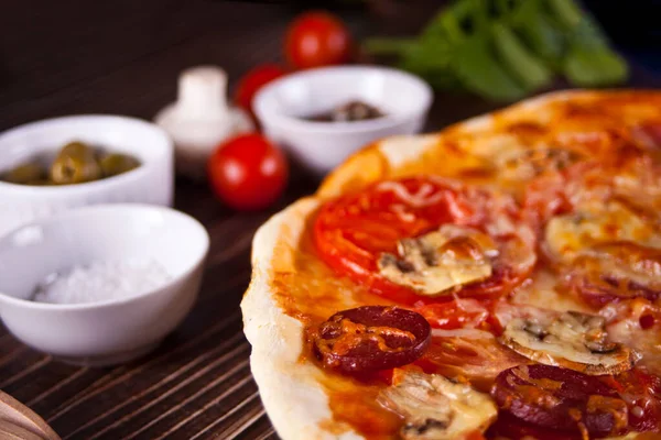 Pizza casera con salchicha de pepperoni, tocino decorado con espinacas e ingredientes en el fondo. — Foto de Stock