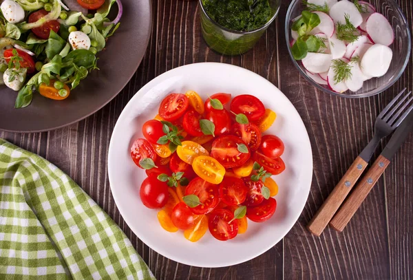 Sallader av färska körsbärstomater, mozzarella, basilika och andra grönsaker på middagsbordet — Stockfoto