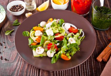 Taze vişneli domates salataları, mozzarella, fesleğen, turp ve diğer sebzeler yemek masasında. Üst görünüm.