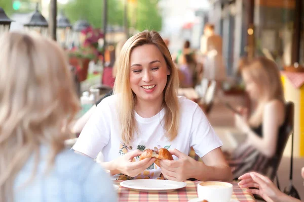 Jovem mulher comendo croissant e bebendo café em um terraço com amigos — Fotografia de Stock