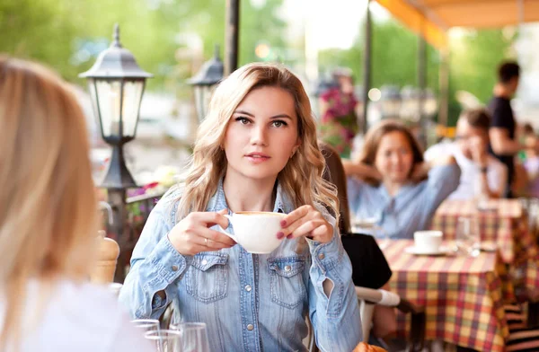 Ung kvinna dricker kaffe på en kafé terrass med vänner — Stockfoto