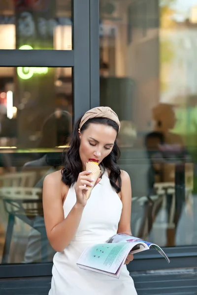Mulher feliz sentado, ler revista e comer um delicioso cone de sorvete — Fotografia de Stock