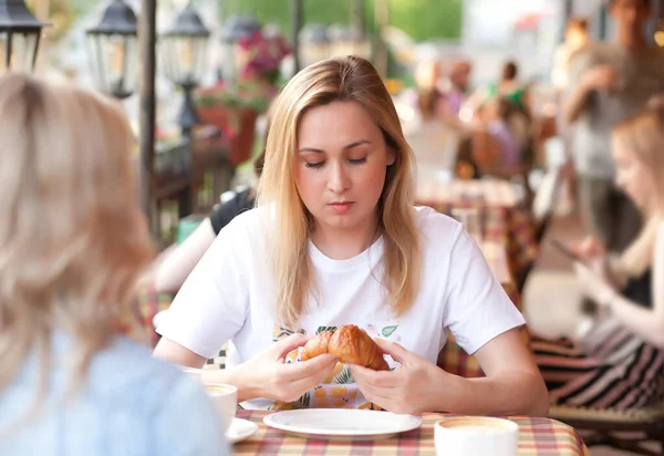 Jovem mulher comendo croissant e bebendo café em um terraço com amigos — Fotografia de Stock