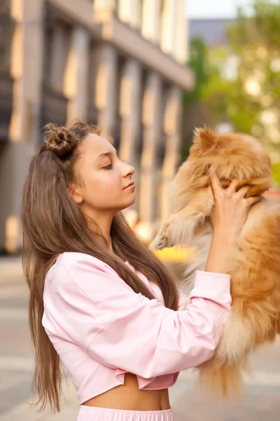 Adolescente chica con animal de compañía perro pequeño sosteniendo en un manos al aire libre en un parque — Foto de Stock