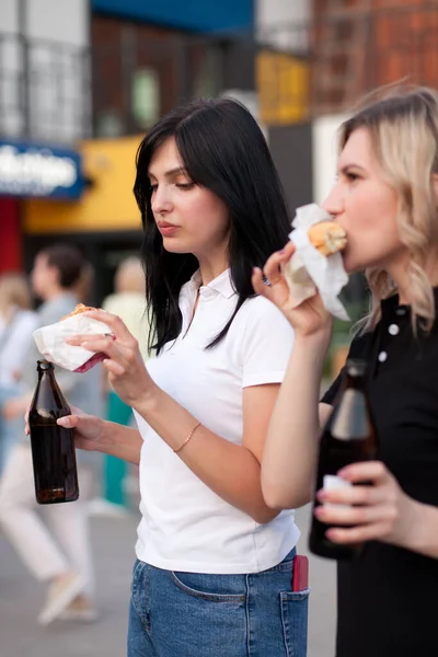 Csinos fiatal nők hamburgert esznek az utcán. — Stock Fotó