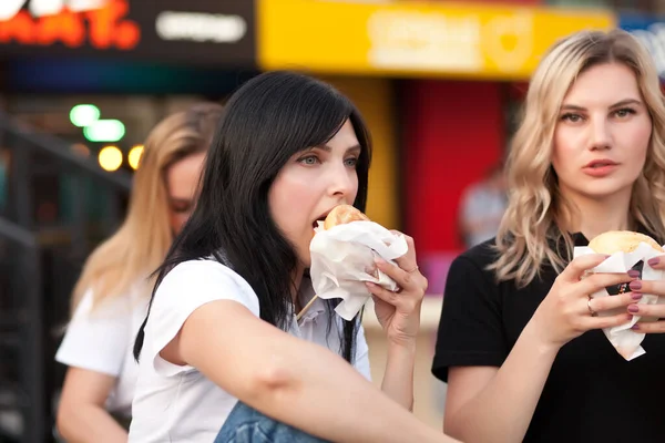 Csinos fiatal nők hamburgert esznek az utcán. — Stock Fotó