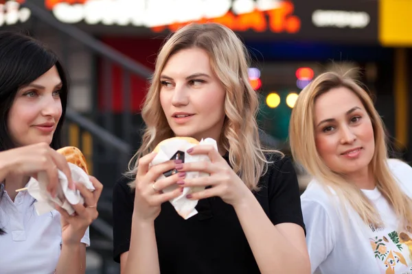 Csinos fiatal nők hamburgert esznek az utcán. — Stock Fotó