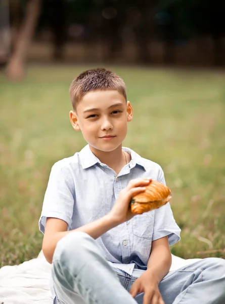 Chlapec sedí na piknik letní dovolenou a jíst čerstvě upečený croissant sendvič — Stock fotografie