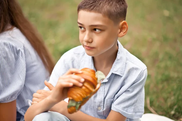 Chłopiec dzieciak siedzi na piknik letnie wakacje i jedzenie świeżo upieczony rogalik kanapka — Zdjęcie stockowe
