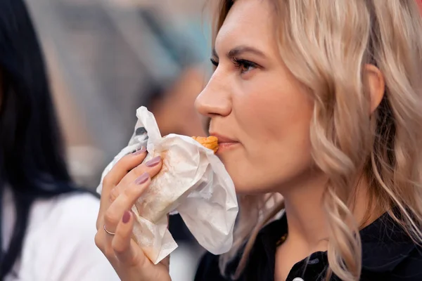 Pretty young woman eating hamburger outdoor on the street — Stock Fotó