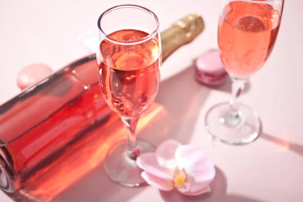 Copa tropical de verano de champán de vino de cóctel rosa con flores de orquídea rosa decoradas con botellas y macarrones. Vista superior. — Foto de Stock