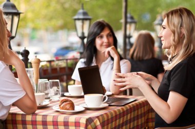 Güzel kadın işçiler ya da öğrenciler kafede dizüstü bilgisayar kullanıyorlar ve konuşuyorlar.