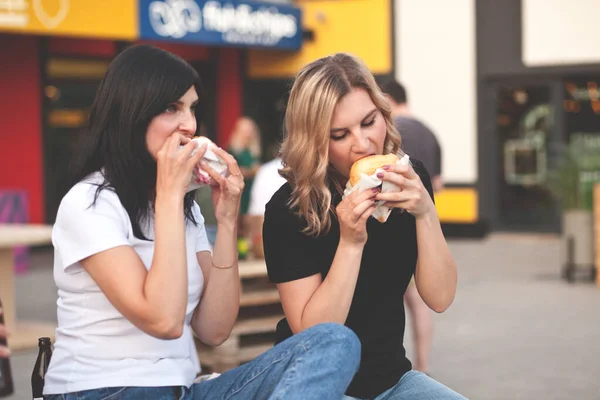 Csinos fiatal nők hamburgert esznek az utcán. — Stock Fotó