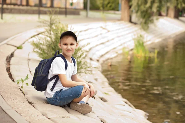 Chłopiec siedzi w pobliżu jeziora lub stawu i relaksujące. Szczęśliwego dzieciństwa. — Zdjęcie stockowe