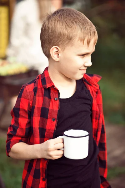 Teen kluk v kostkované košili drží šálek pití. Cestování, túra, dovolená, koncept kempování. — Stock fotografie