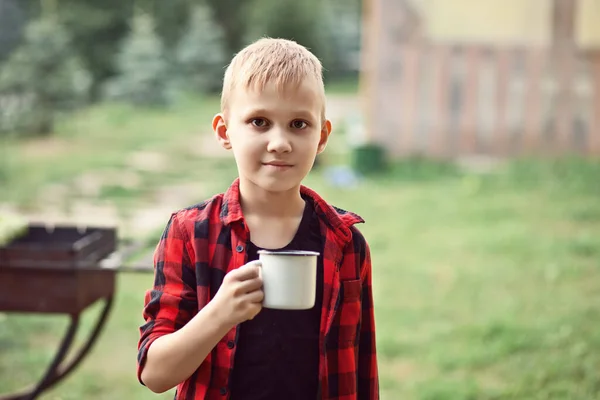 Teen boy kid in kariertem Hemd hält eine Tasse mit Getränken. Reisen, Wandern, Urlaub, Campingkonzept. — Stockfoto