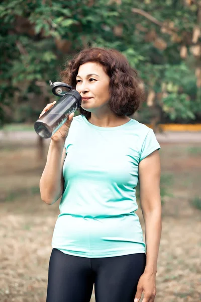 Middle age senior runner woman drinking bottled water after fitness exercise outdoors