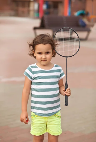 Маленька чарівна дівчинка тримає бадмінтонну ракетку і посміхається. Активна гра на відкритому повітрі . — стокове фото