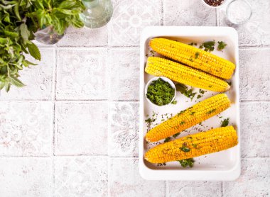 Fırında pişmiş mısır koçanı otlu, tereyağı beyaz tepside.