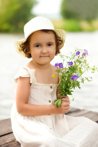 Menina feliz sentada com um buquê de flores silvestres. Verão país vida. — Fotografia de Stock